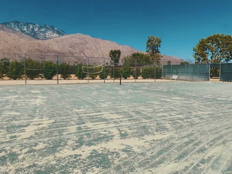 A clay court being prepared for scarifying, mountains behind