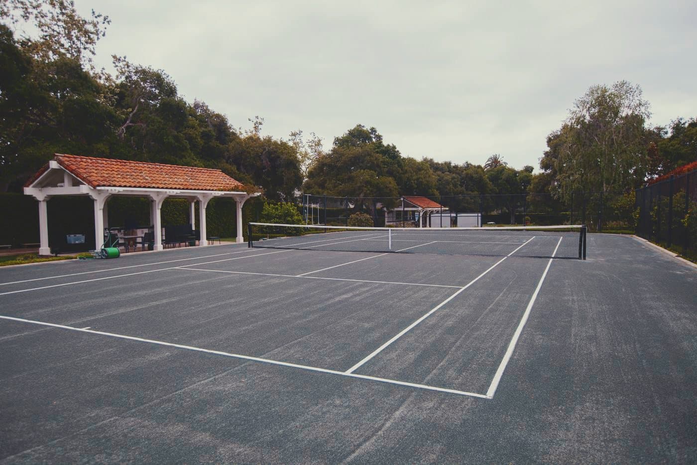 A finished clay court with a tile-roofed pavilion beyond the far baseline