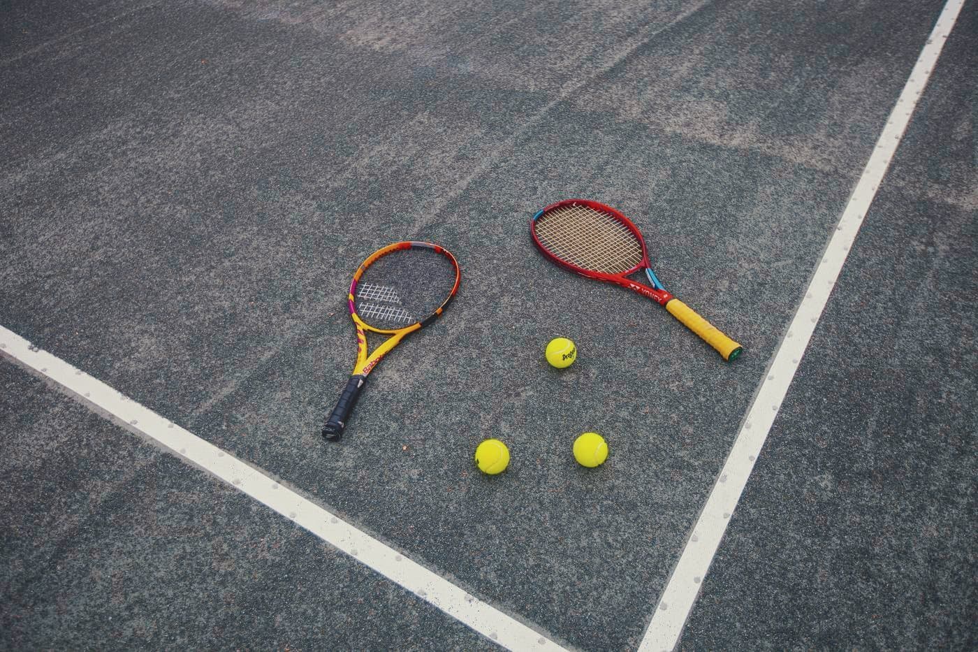 Two rackets and tennis balls resting on freshly lined clay
